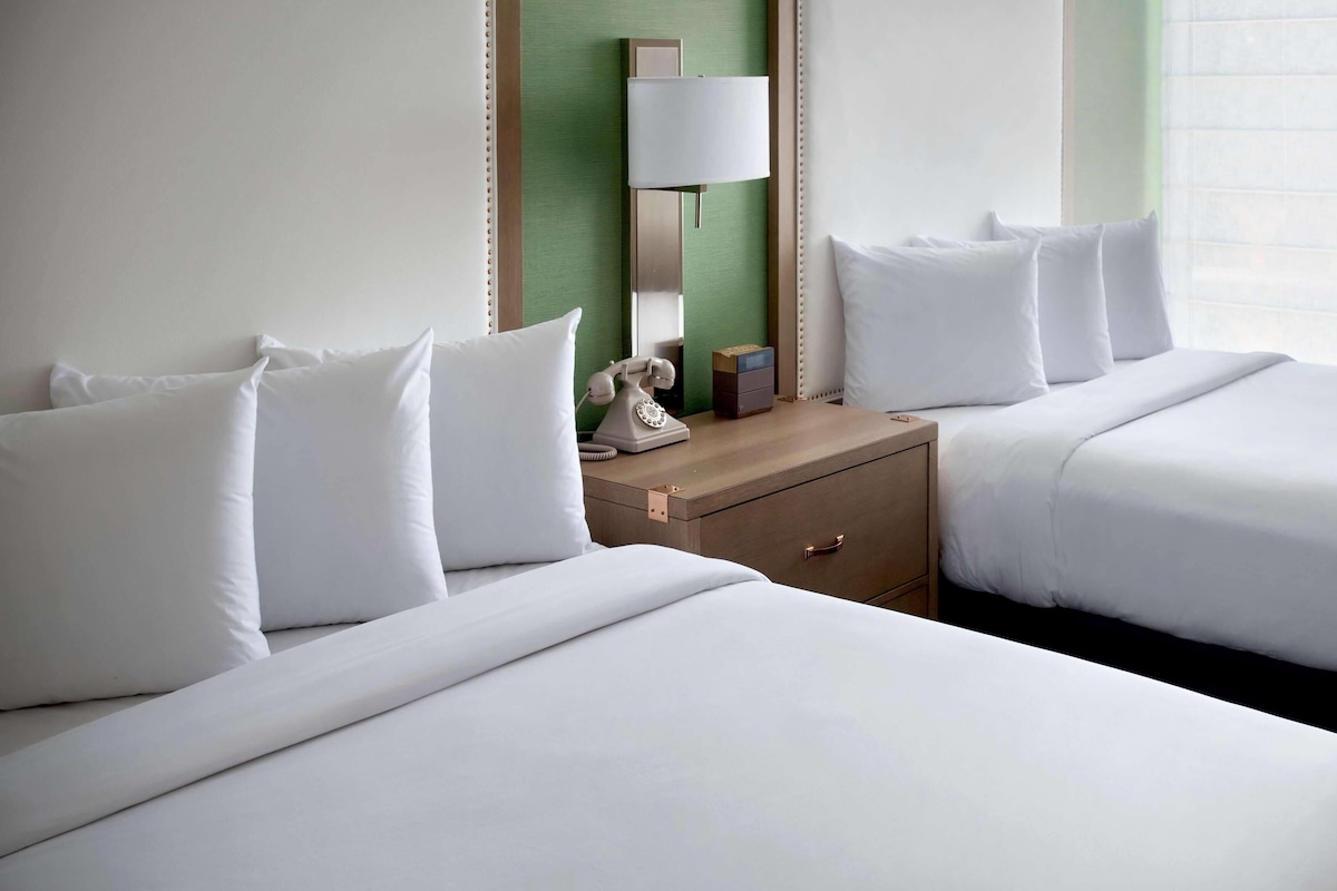 A hotel room with two beds, a bedside table with a lamp, and a telephone.