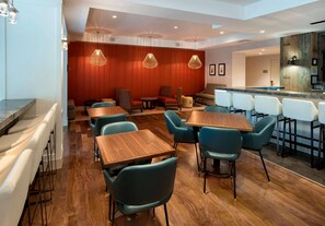 A modern restaurant with wooden tables and chairs, a bar area, and a red accent wall. - The Hayes Street Hotel, Trademark Collection by Wyndham (Nashville)