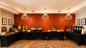 A breakfast buffet setup with a variety of food items and beverages, a waffle station, and decorative lighting. - The Hayes Street Hotel, Trademark Collection by Wyndham (Nashville)