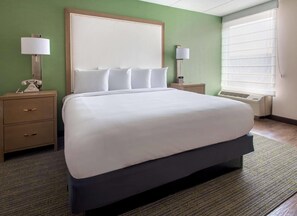 Habitación de hotel con una cama grande, dos mesitas de noche, cabecera y una ventana con persianas.
