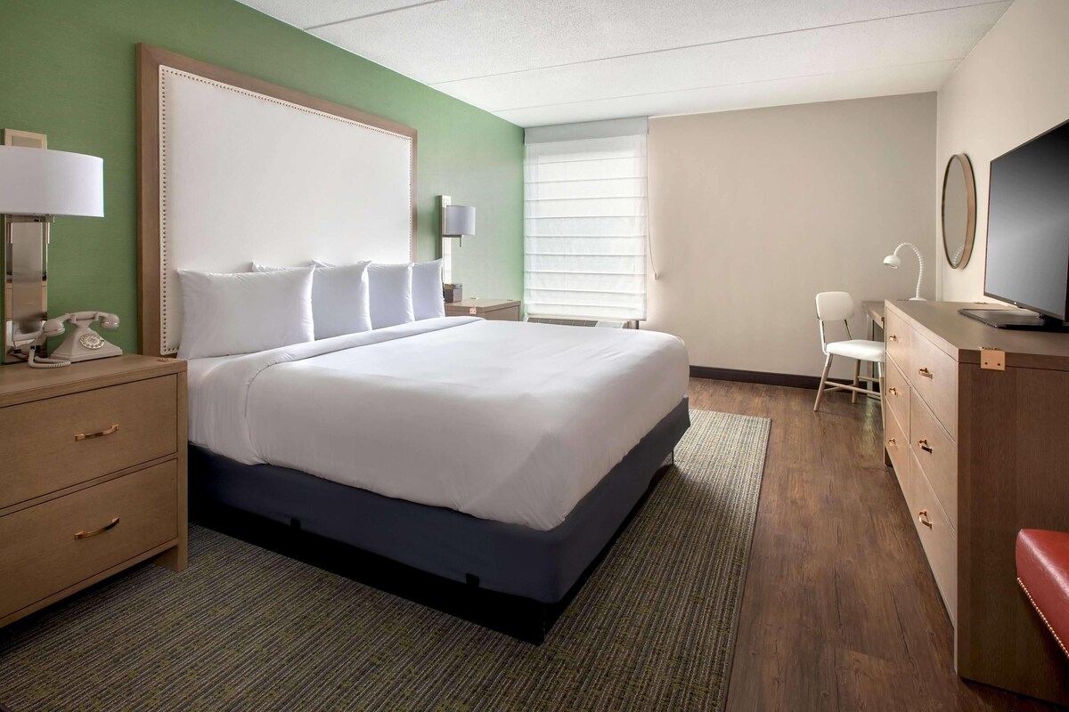 A hotel room with a large bed, bedside tables, a desk, a chair, and a television.