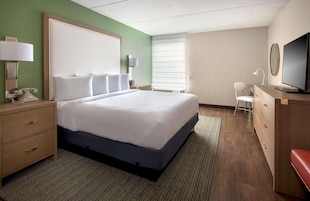 A hotel room with a large bed, bedside tables, a desk, a chair, and a television.