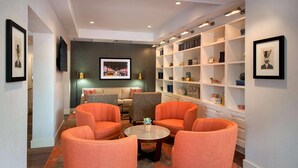 A modern lounge area with orange armchairs, a round coffee table, and a bookshelf with various items. - The Hayes Street Hotel, Trademark Collection by Wyndham (Nashville)