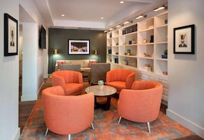 A modern lounge area with orange armchairs, a round coffee table, and a bookshelf with various items.