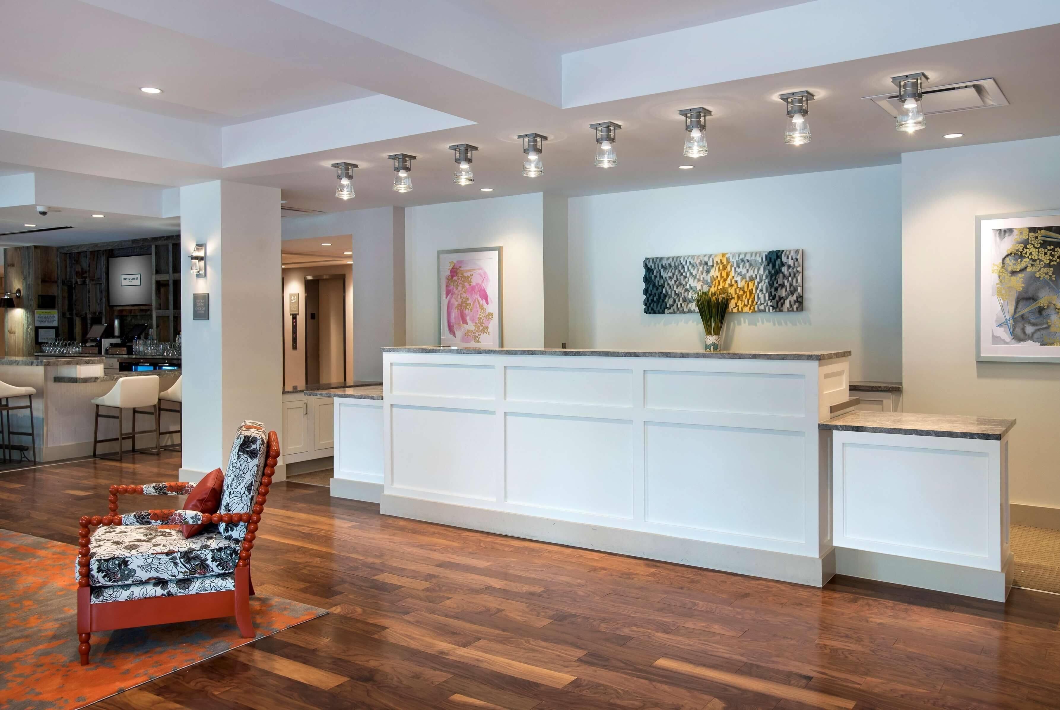 A hotel lobby with a reception desk, a bar area, and a seating area with a patterned armchair.