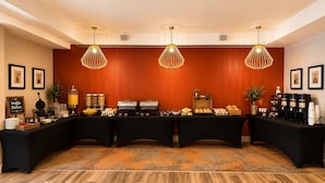 Montaje de un bufé de desayuno con varias estaciones de comida, una barra de café e iluminación decorativa.