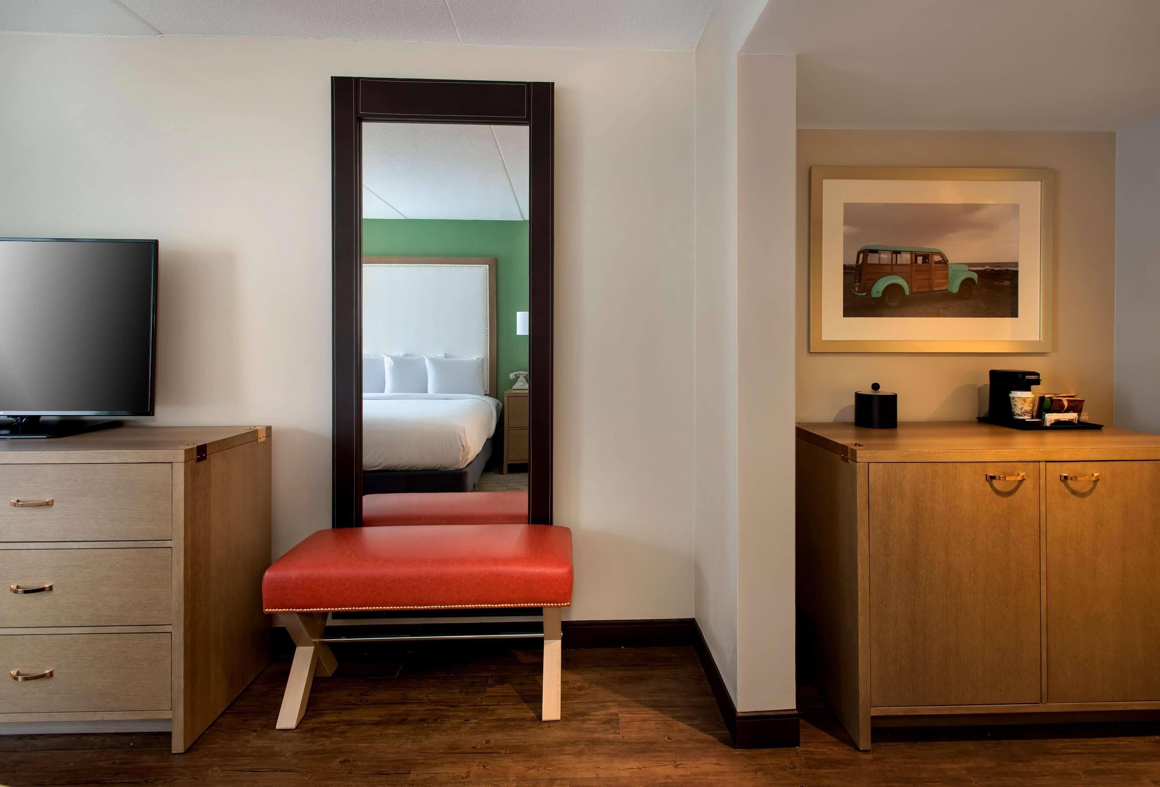 A hotel room with a bed, a television, a bench, a cabinet, and a framed picture on the wall.