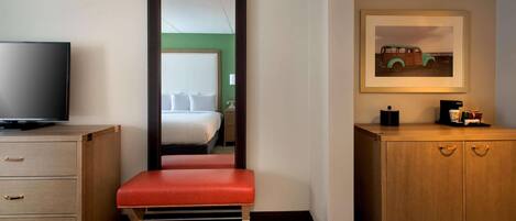 A hotel room with a bed, a television, a bench, a cabinet, and a framed picture on the wall.