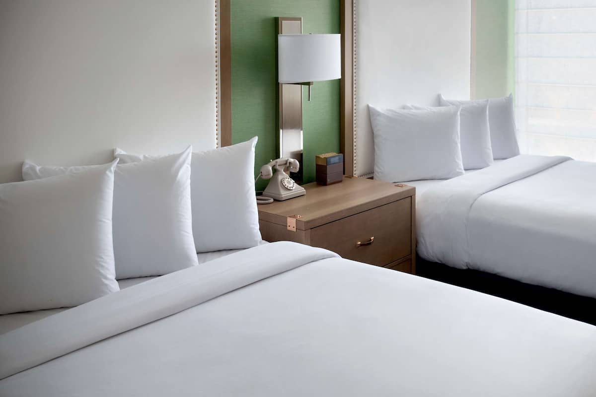 Habitación de hotel con dos camas, una mesita de noche, una lámpara y un teléfono.