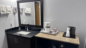 A modern bathroom with a black vanity, a large mirror, a coffee maker, and a towel rack.