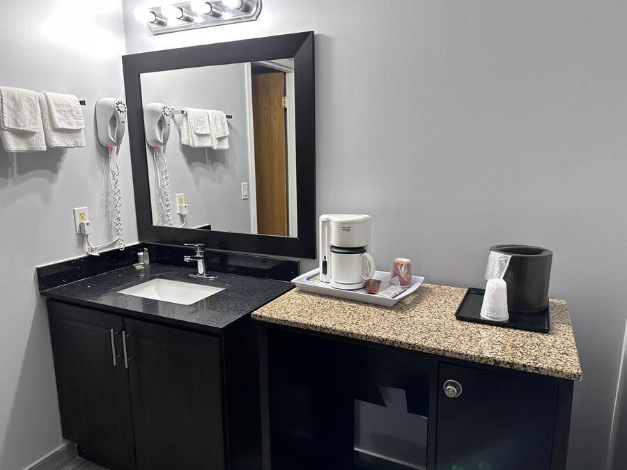 Un baño moderno con tocador negro, un espejo grande, una cafetera y un perchero para toallas.
