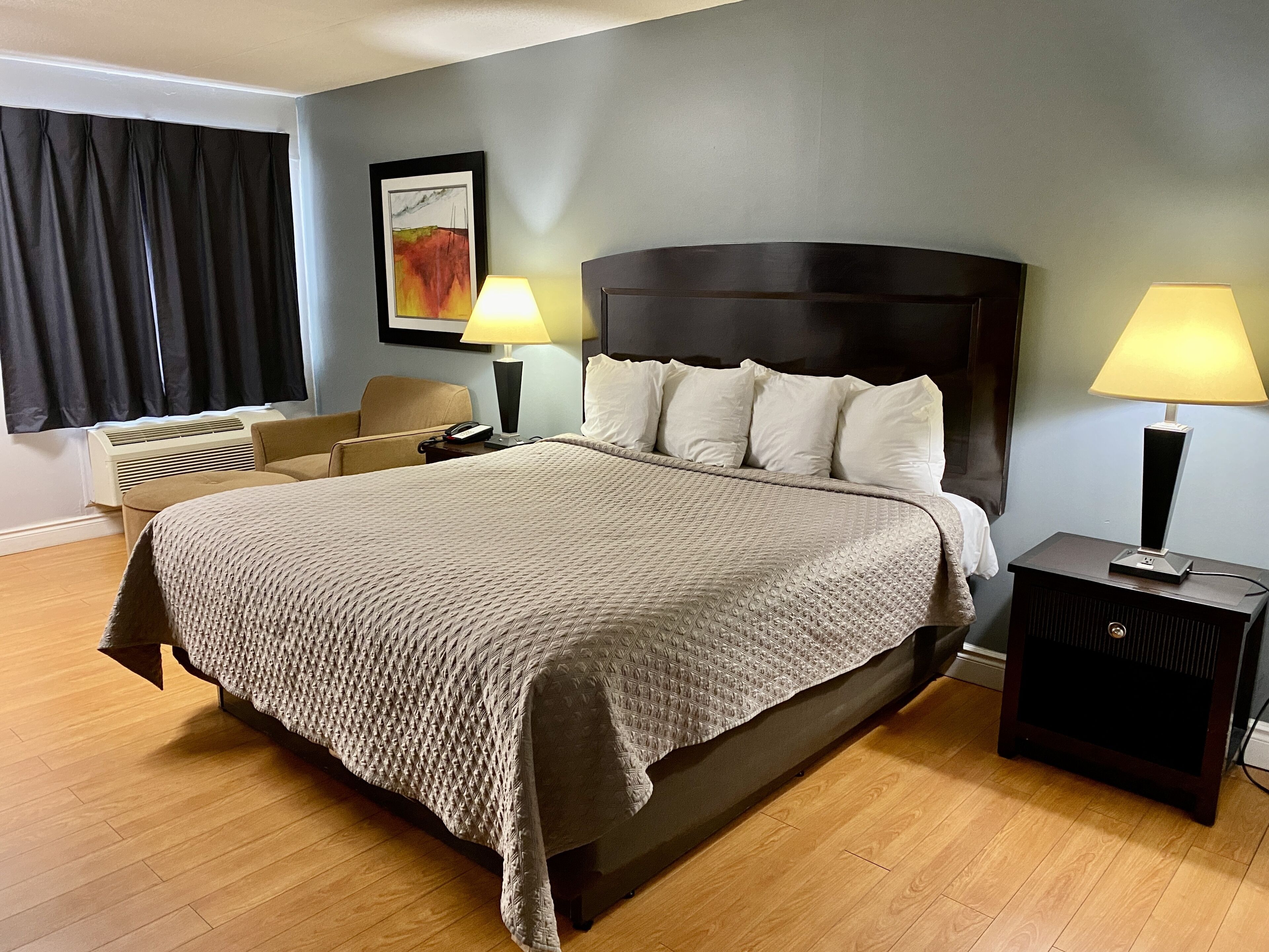 A hotel room with a large bed, two bedside lamps, a chair, a painting on the wall, and a heater.