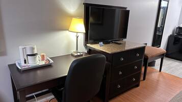 A hotel room with a desk, a chair, a television, a coffee maker, and a lamp.