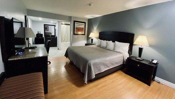 A hotel room with a bed, bedside tables, a desk, a chair, and a bathroom visible through an open door.