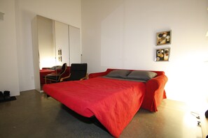 A bedroom with a bed, a chair, a desk, and a wardrobe. - Downtown Loft Style Condo Heated Parking (Saskatoon)
