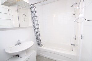 A modern bathroom with a white sink, a bathtub, and a shower curtain. - Downtown Loft Style Condo Heated Parking (Saskatoon)