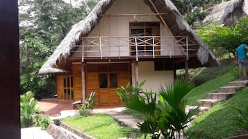 A thatched-roof house with a wooden porch and a small garden area.