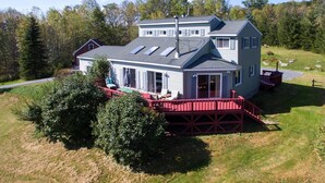A two-story house with a red deck, large windows, and a chimney.