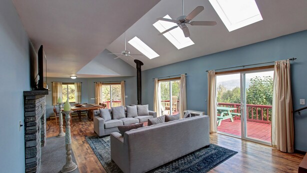 A spacious living room with a large sofa, a fireplace, and a balcony with a wooden deck.