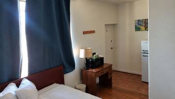 Quarto de hotel com cama, escrivaninha, luminária, micro-ondas e geladeira.