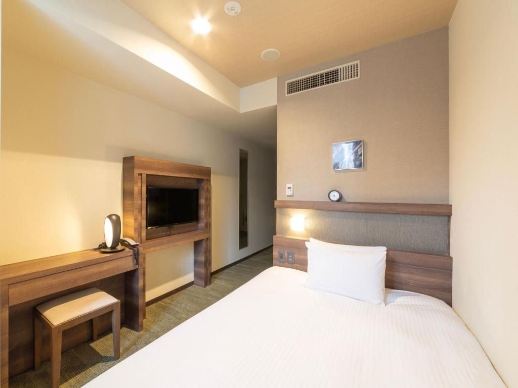 A hotel room with a bed, a desk, a television, and a wall-mounted clock.