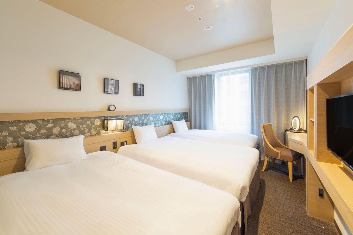 Een hotelkamer met twee bedden, een bureau met een televisie, een lamp en een raam met gordijnen.