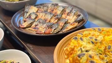 A table with various dishes including grilled fish, a vegetable dish, and a baked dish with beans and vegetables.