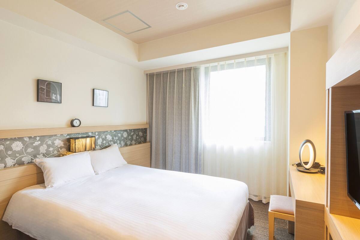 Een hotelkamer met een groot bed, een bureau met stoel, een televisie en een raam met gordijnen.