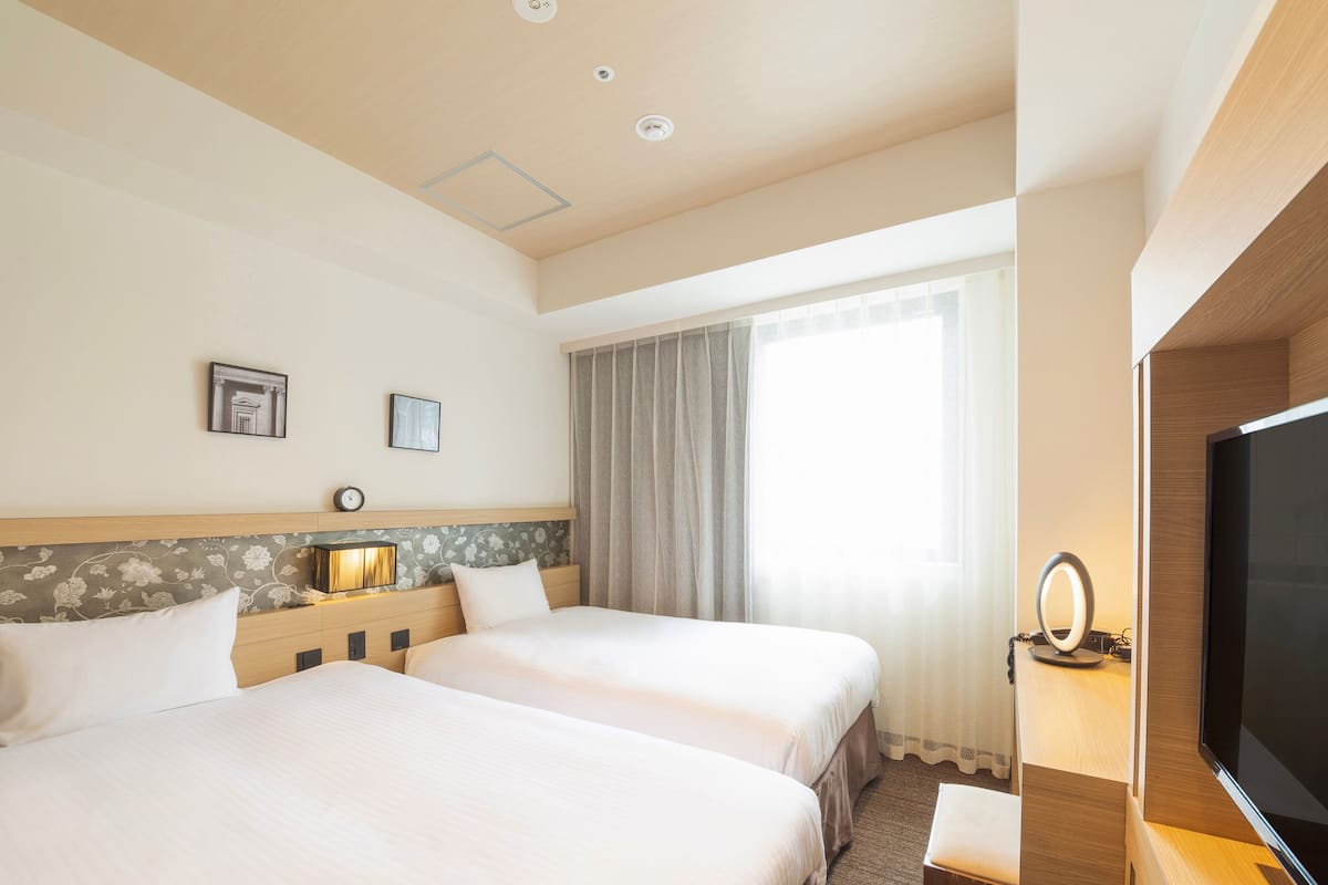 Een hotelkamer met twee bedden, een televisie, een bureau met lamp en een raam met gordijnen.
