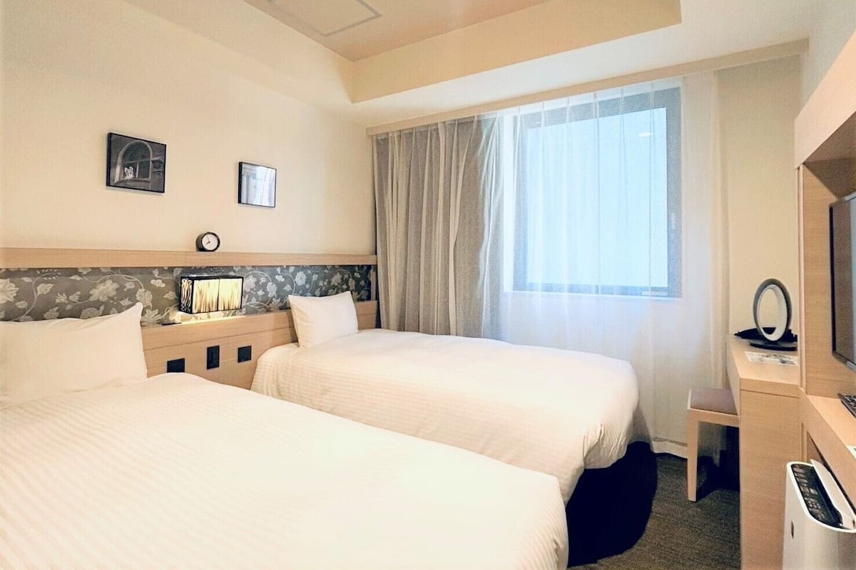 Een hotelkamer met twee bedden, een bureau met een computer, een televisie en een raam met gordijnen.