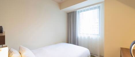 A hotel room with a bed, a desk with a chair, a mirror, and a window with curtains.