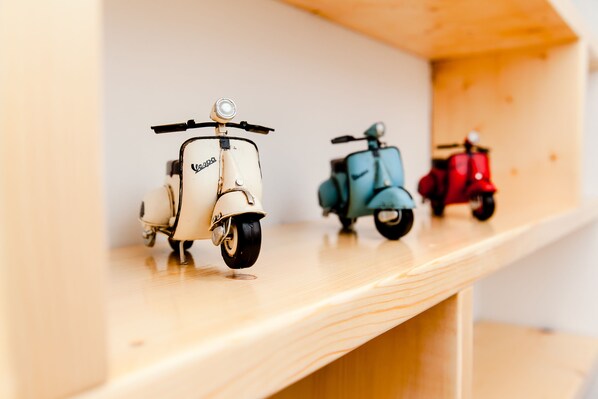 Three vintage toy scooters on a wooden shelf.