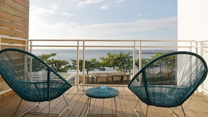 A wooden deck with two green wicker chairs and a small table, overlooking a beach and ocean. - Hooope Inn (Checheng)