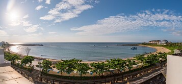 Vista costera con playa, muelle y un edificio grande con estructura en forma de cúpula.