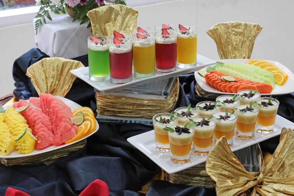 Une table de buffet proposant une variété de plats et de boissons, notamment des fruits et des légumes coupés en tranches, ainsi que des boissons à plusieurs couches.