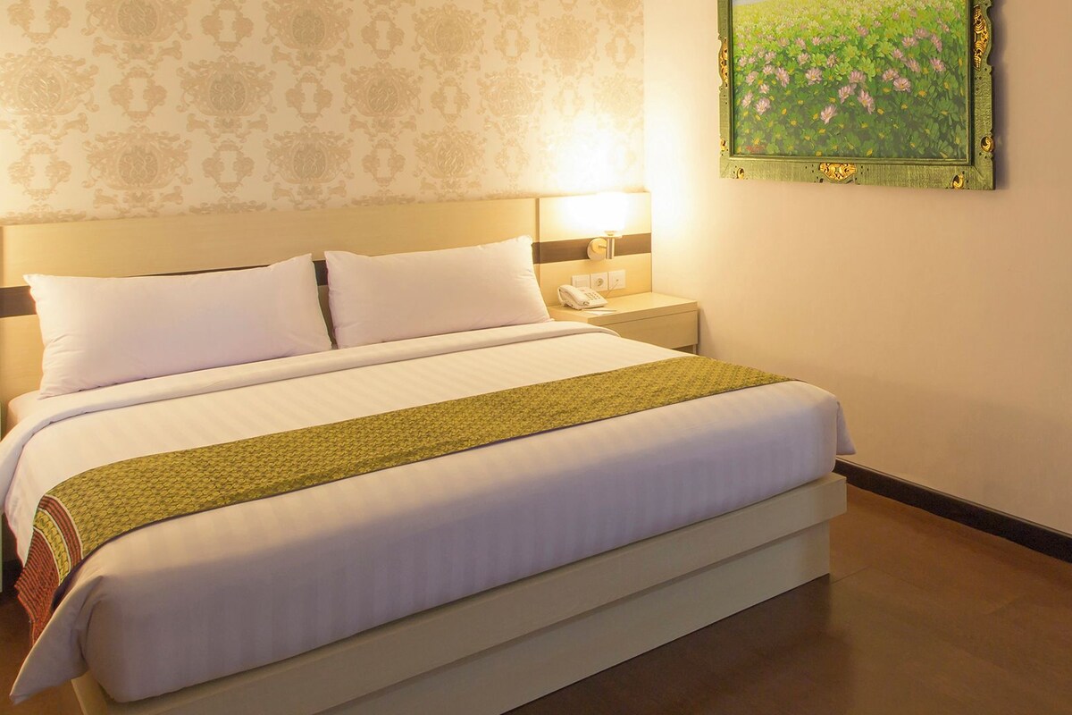 Een hotelkamer met een groot bed, een nachtkastje, een lamp en een lijst met een afbeelding aan de muur.