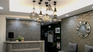 A reception area with a metal mesh counter, grey upholstered chairs, and a decorative wall with a hexagonal mirror. - Ortigas Budget Hotel - Kapitolyo (Pasig)