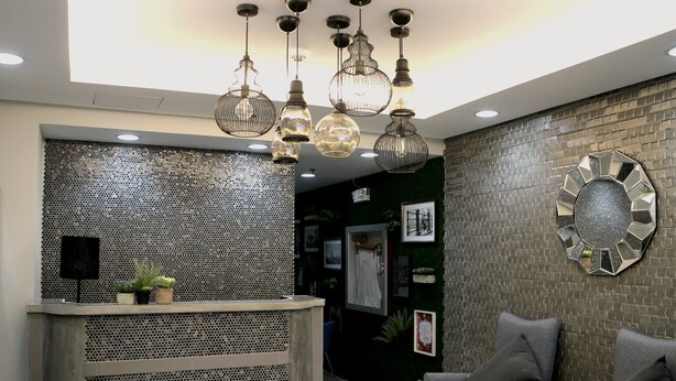 A reception area with a metal mesh counter, grey upholstered chairs, and a decorative wall with a hexagonal mirror. - Ortigas Budget Hotel - Kapitolyo (Pasig)
