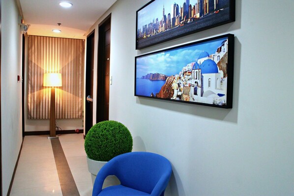A hallway with a blue chair, a potted plant, and two framed pictures of cityscapes.