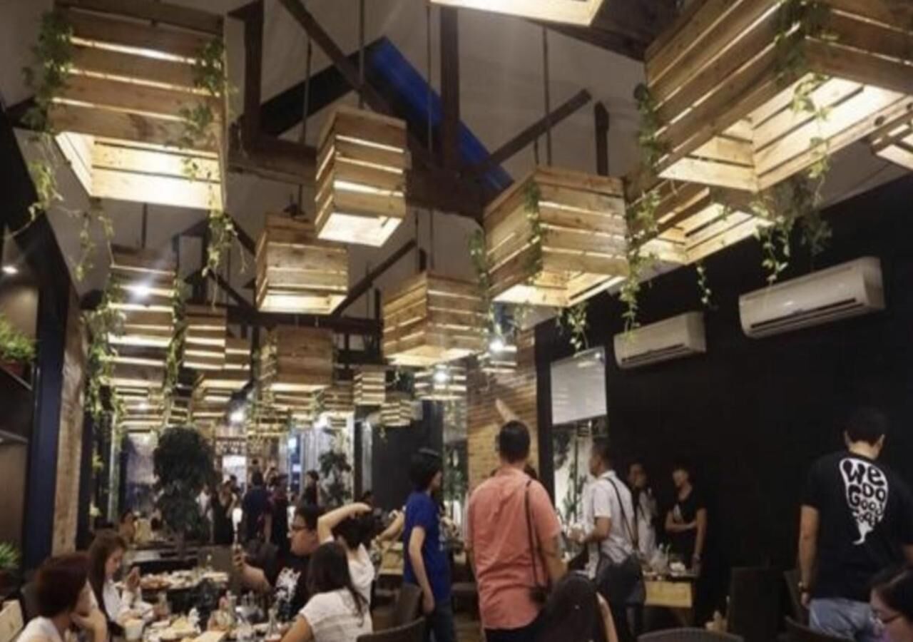 Un restaurante con vigas de madera en el techo, plantas colgantes y comensales.