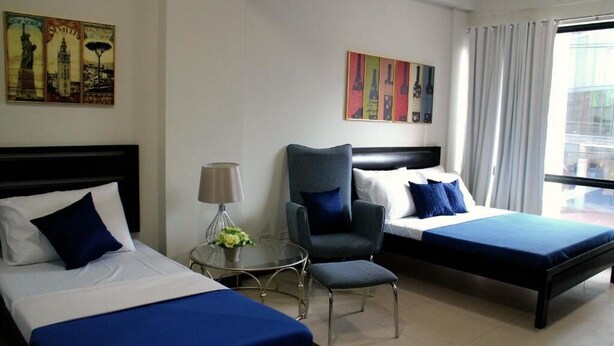 A hotel room with two beds, a chair, a table with a lamp, and artwork on the walls. - Ortigas Budget Hotel - Kapitolyo (Pasig)