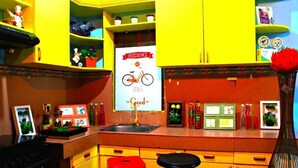 A kitchen with yellow cabinets, a red stool, a black stool, and a sign that says "Riding makes good food." - Panglao Island Inn - Hostel (Panglao)