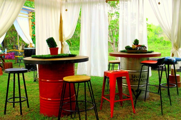 An outdoor patio with a round table, red stools, and potted plants. - Sea Breeze Hostel (Panglao)