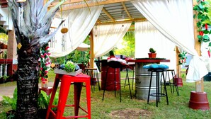Un patio al aire libre con una pérgola de madera, cortinas blancas y taburetes rojos.