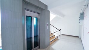 Un ascenseur moderne doté de portes en verre, un escalier avec des marches en bois et un sol carrelé de couleur blanche.