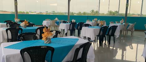 Un área de comedor al aire libre techada con mesas dispuestas para dos, con manteles blancos y detalles en azul.