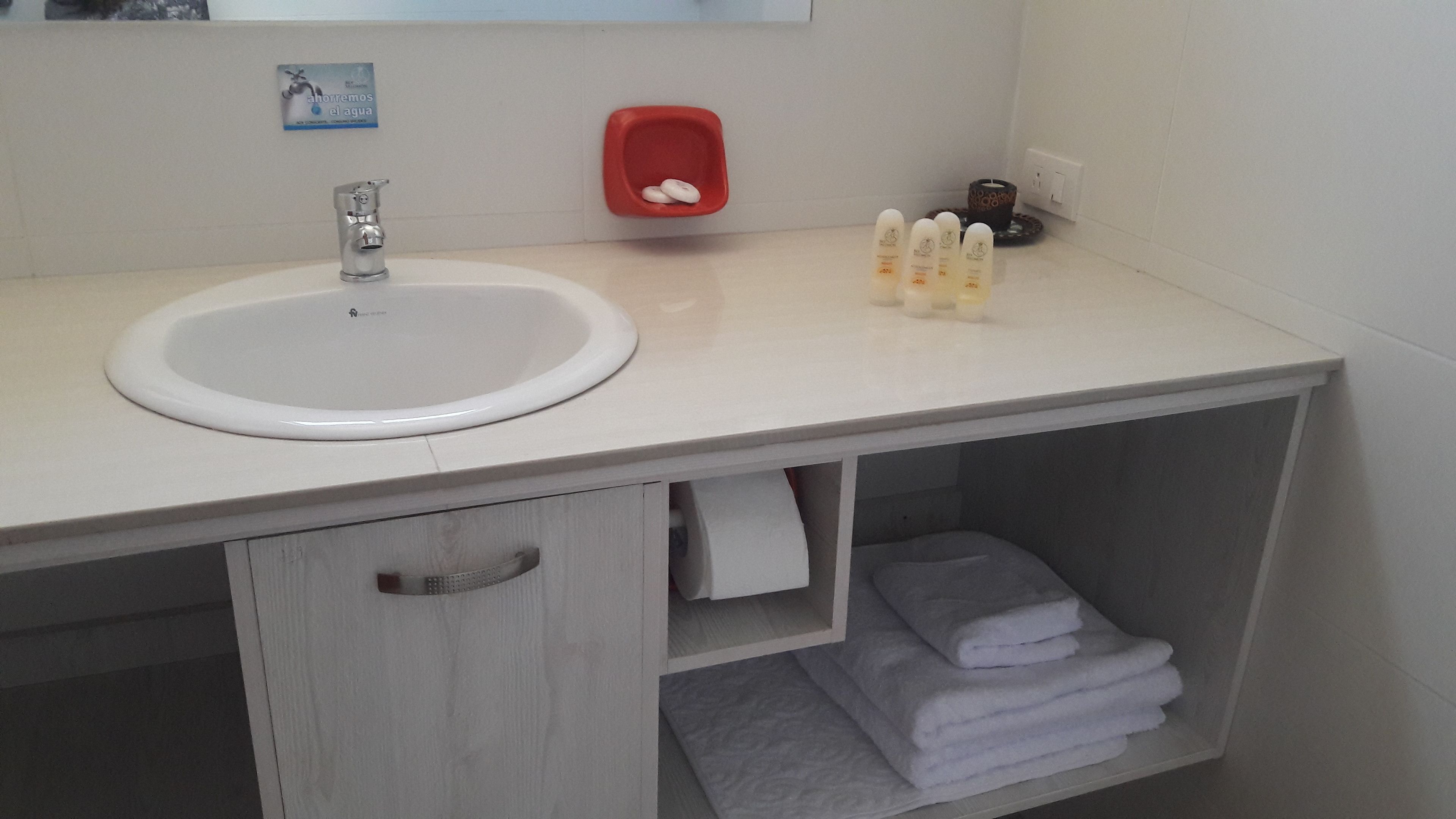 Un baño con un lavamanos blanco, un dispensador de jabón rojo y un perchero para toallas.