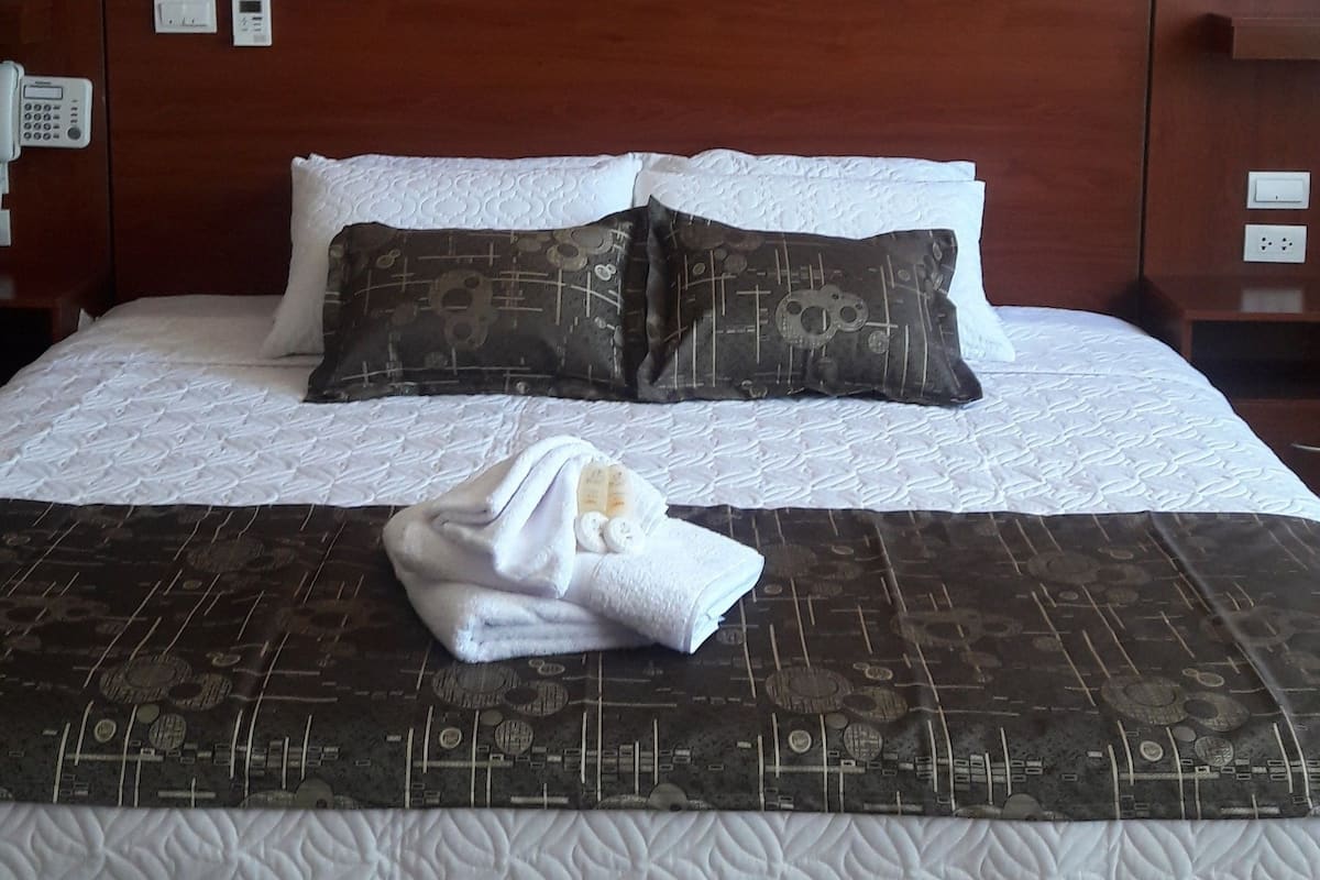 Una cama bien tendida con ropa de cama estampada, una almohada blanca y una toalla doblada sobre la cama.