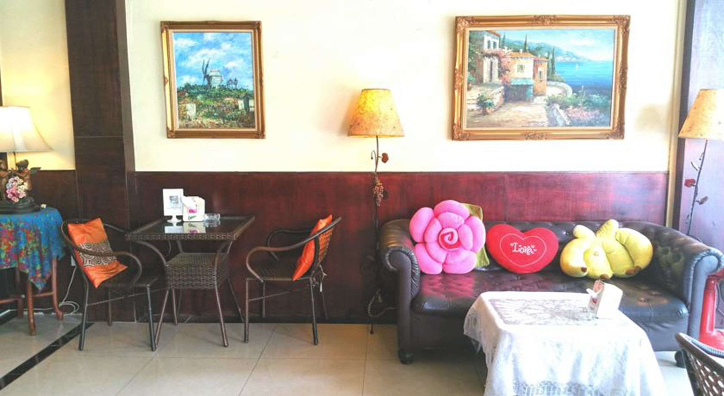 Une pièce comprenant un coin repas avec une table et des chaises, un canapé agrémenté de coussins décoratifs et deux tableaux encadrés accrochés au mur.