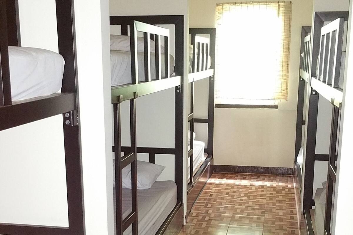 A corridor with bunk beds, a window with blinds, and an air conditioning unit on the wall.